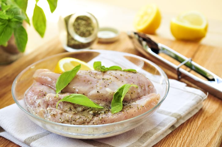 Marinated chicken breasts in a bowl withs seasonings